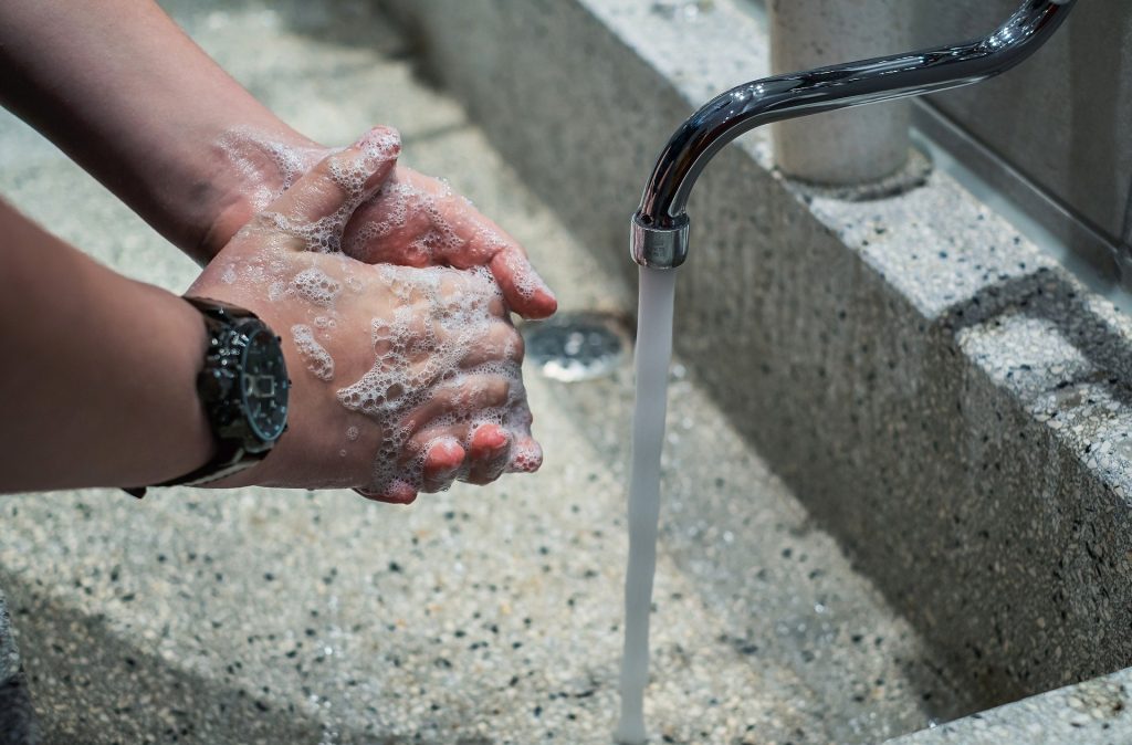 man washing hands at running faucet